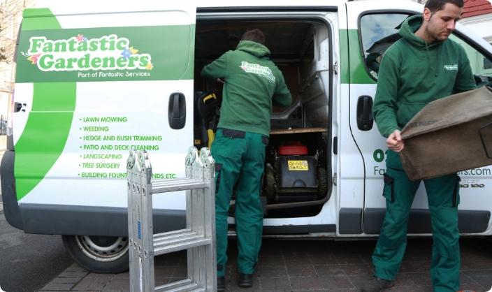The image shows the side of a Fantastic Gardeners branded van that is being loaded by a gardener wearing a green uniform.